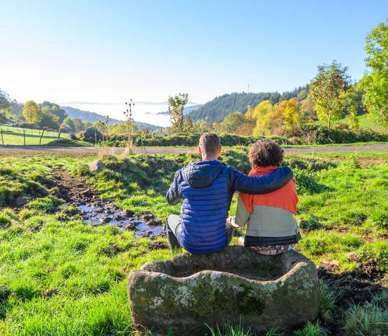 Jeunes assis sur un rocher, admirant la nature dans les Hautes Terres du Cantal.