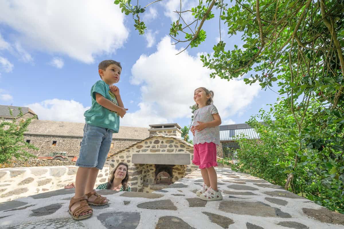 Enfants jouant près d'une cheminée extérieure en pierre dans un cadre naturel.