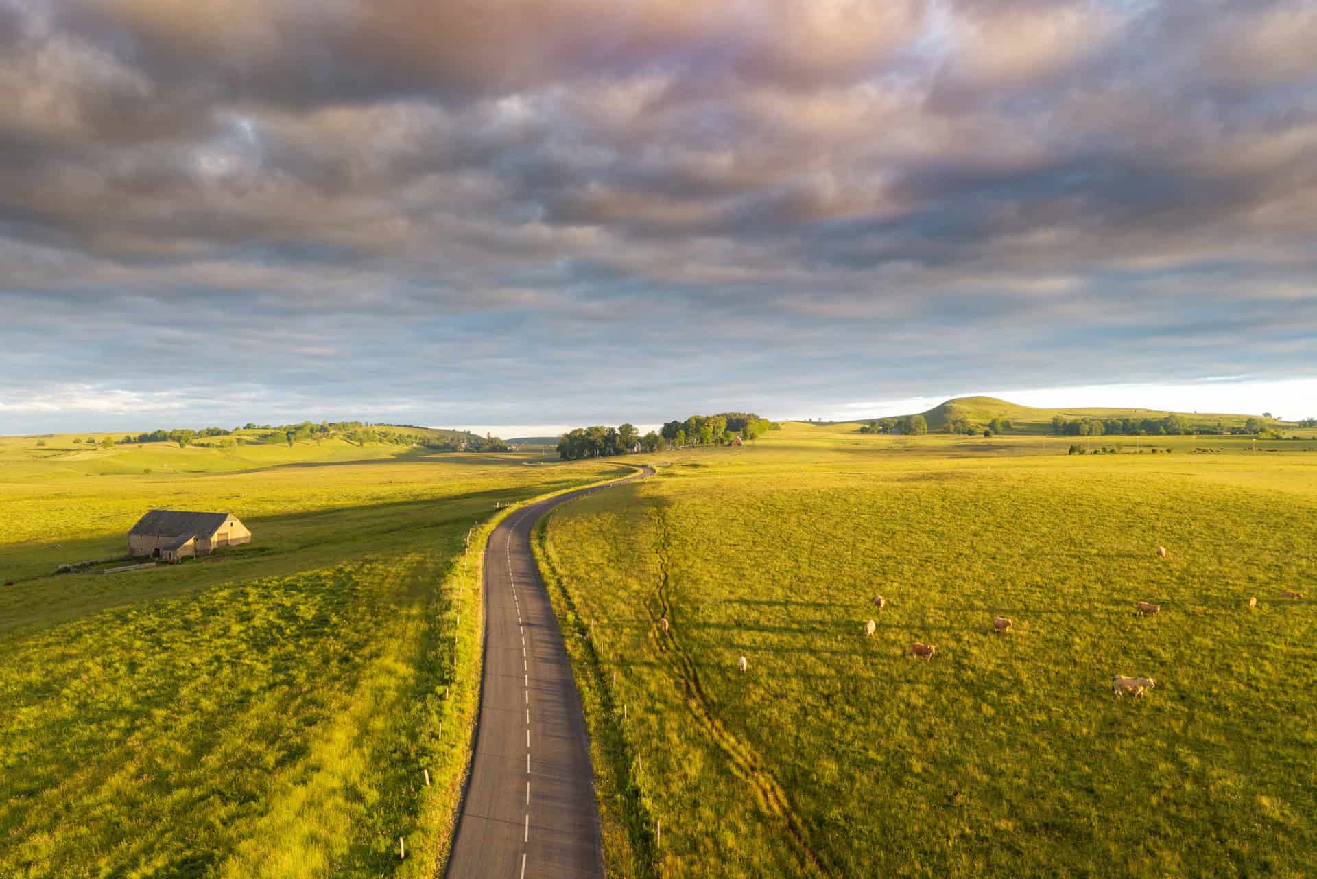 Paysage rural avec route sinueuse et champs verdoyants sous ciel nuageux.