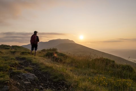 Randonneur contemplant le coucher de soleil sur une montagne dans les Hautes Terres.