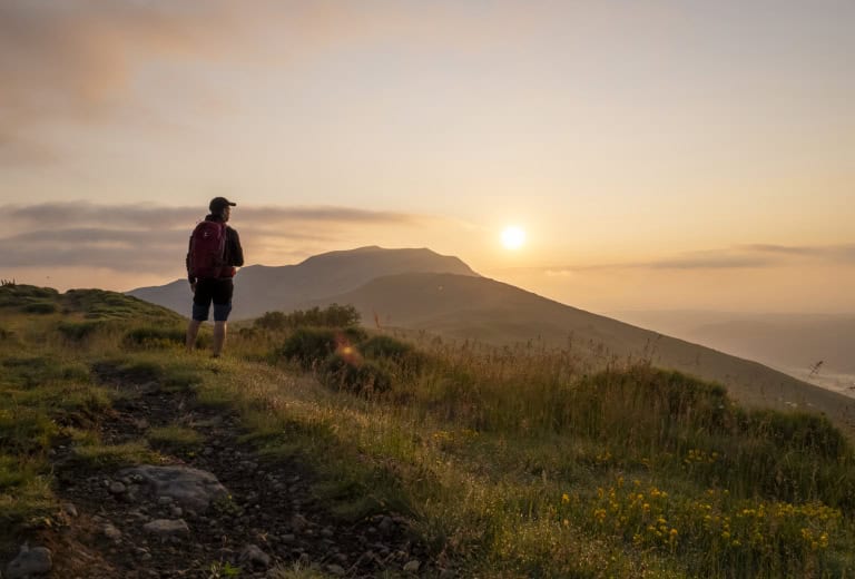 Randonneur contemplant le coucher de soleil sur une montagne dans les Hautes Terres.
