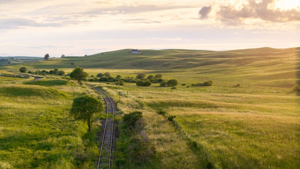 Paysage rural avec train et collines au coucher du soleil.