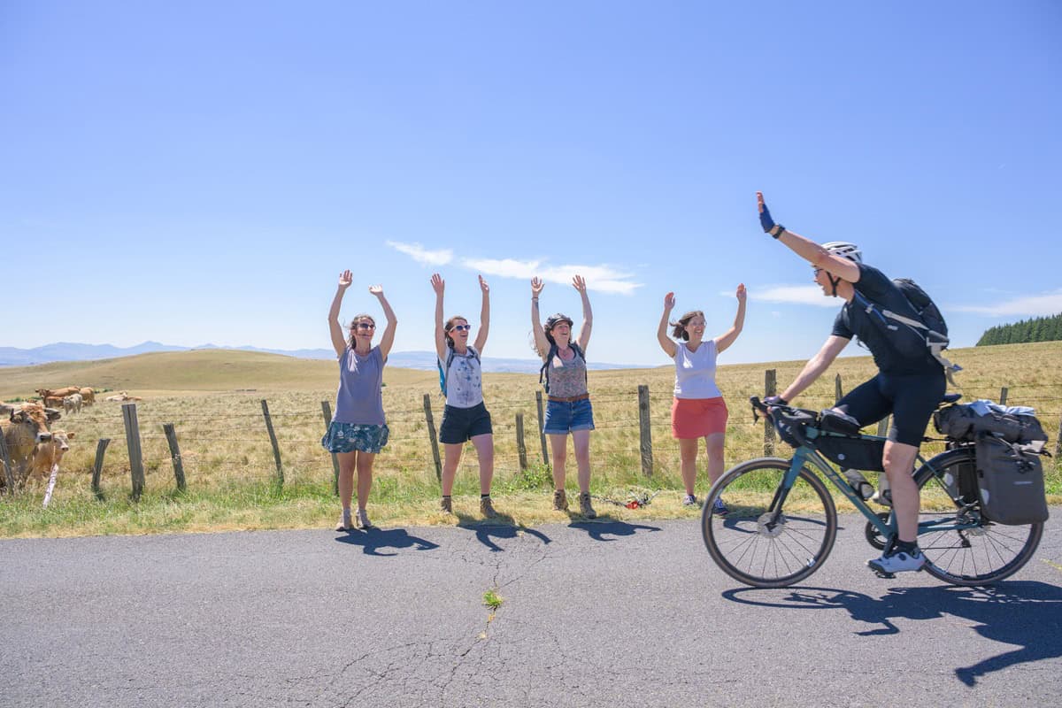 Cycliste saluant un groupe de randonneurs dans un paysage rural.