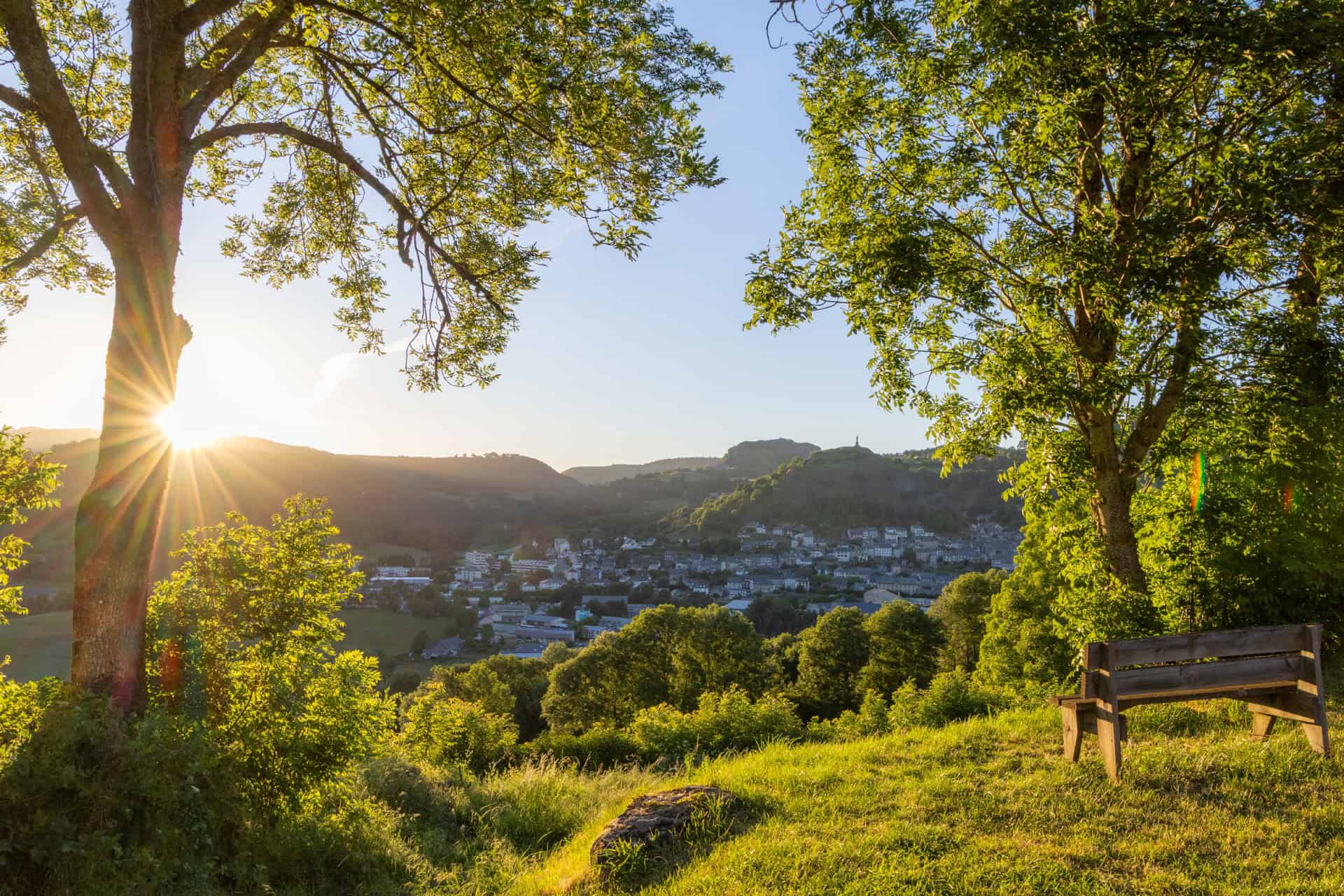 Paysage naturel avec arbres, soleil couchant et vue sur un village dans les montagnes du Cantal.